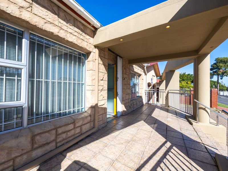 A covered outdoor patio area featuring stone-clad walls, tiled flooring, and metal security railings, providing a sheltered entrance space.