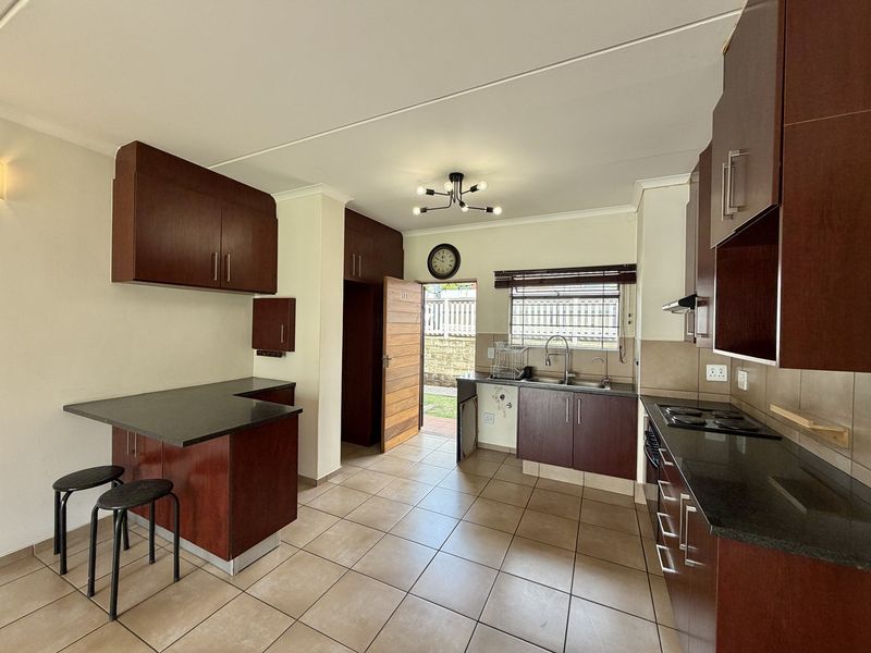 Functional kitchen featuring dark wood cabinetry, granite countertops, an electric hob, and a breakfast nook, with direct access to an outdoor area.