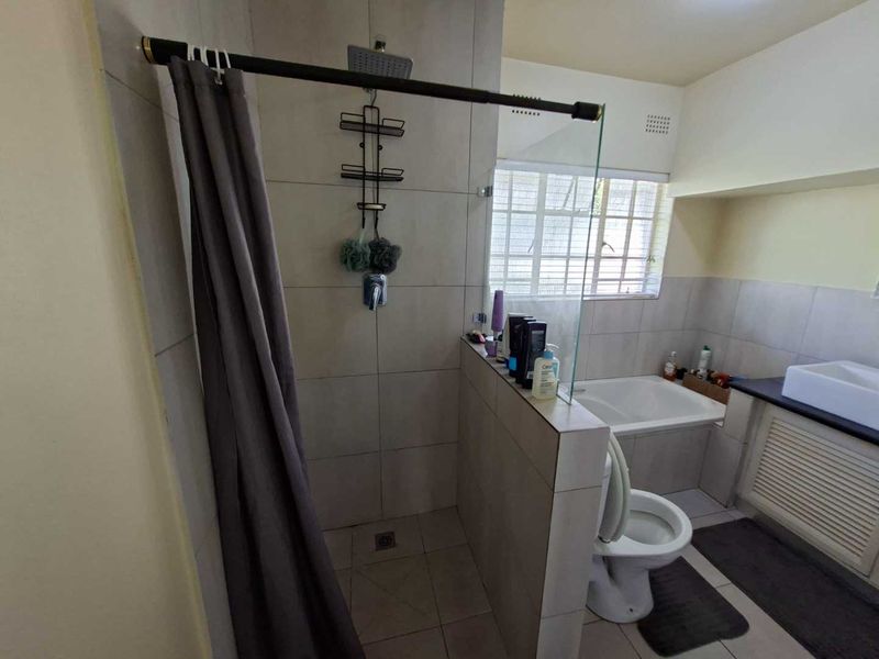 A functional bathroom featuring a walk-in shower with glass screen, built-in bathtub, toilet, and vanity cabinet with basin.