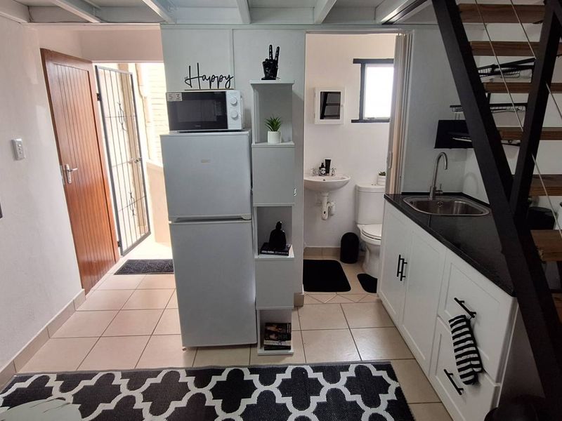 Compact open-plan living area featuring a kitchenette with built-in cabinetry, tiled flooring, and a staircase leading to an upper level.