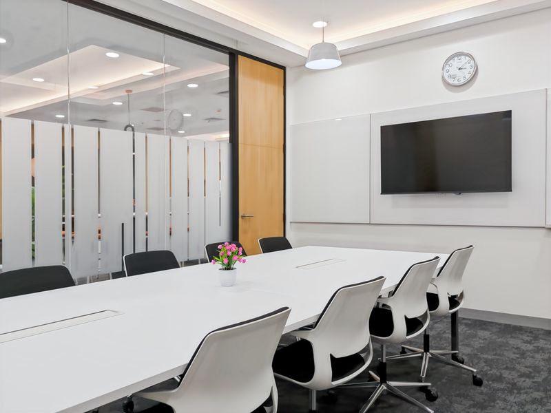 A modern, well-lit office meeting room featuring a glass partition, whiteboard, and professional carpet flooring.