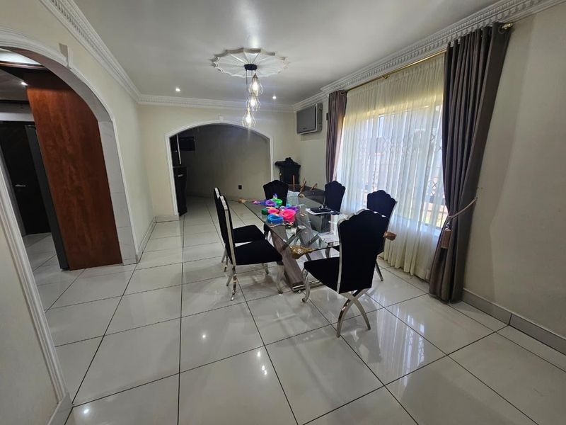 A bright dining room featuring polished porcelain floor tiles, decorative ceiling rose, and an elegant archway leading to adjacent living spaces.
