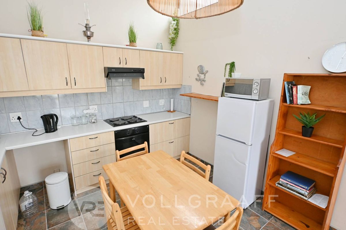 A functional kitchen featuring light wood cabinetry, a built-in oven, hob, extractor fan, and tiled splashbacks, with an adjacent dining area.
