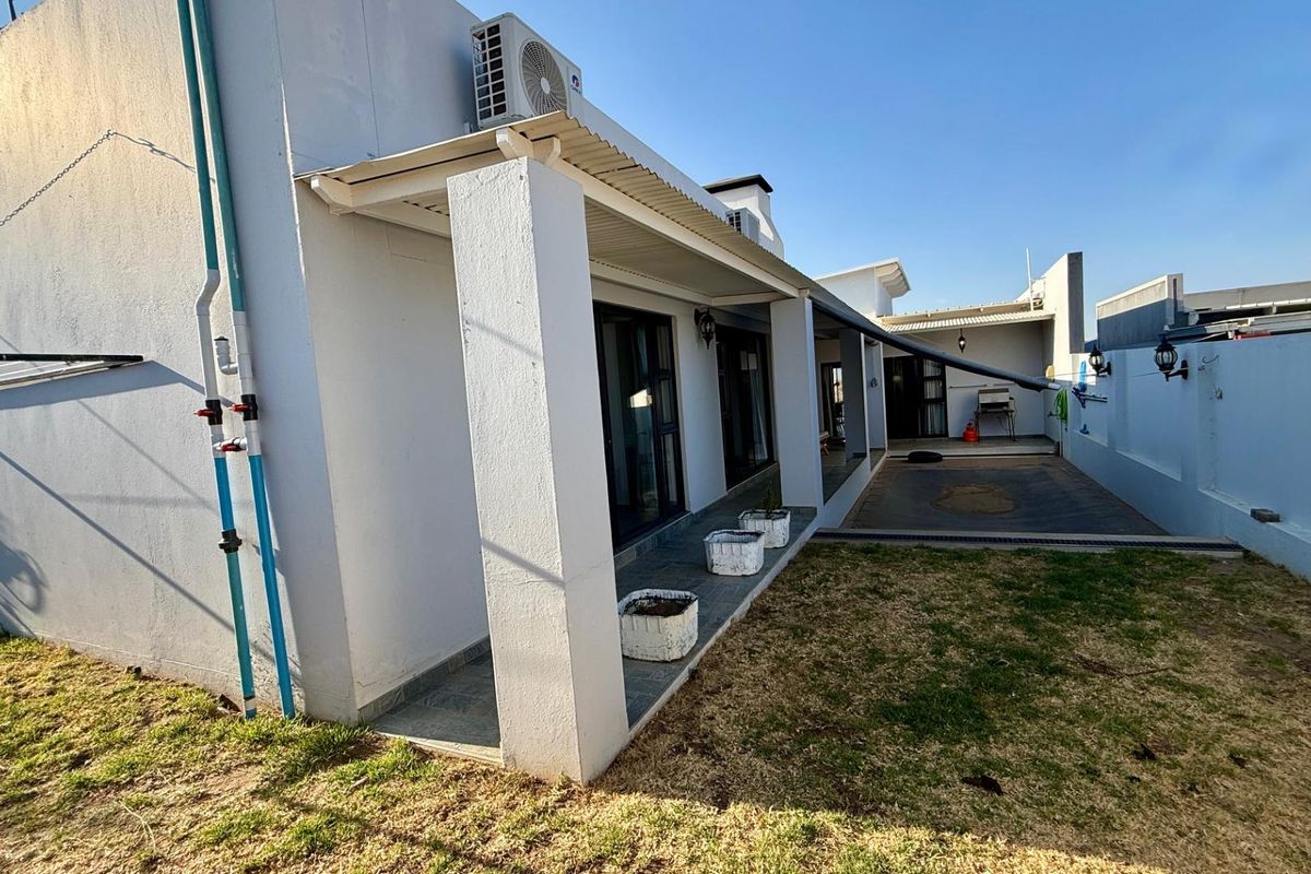 Rear view of the property featuring a covered patio area, tiled flooring, wall-mounted air conditioning unit, and a small garden space.
