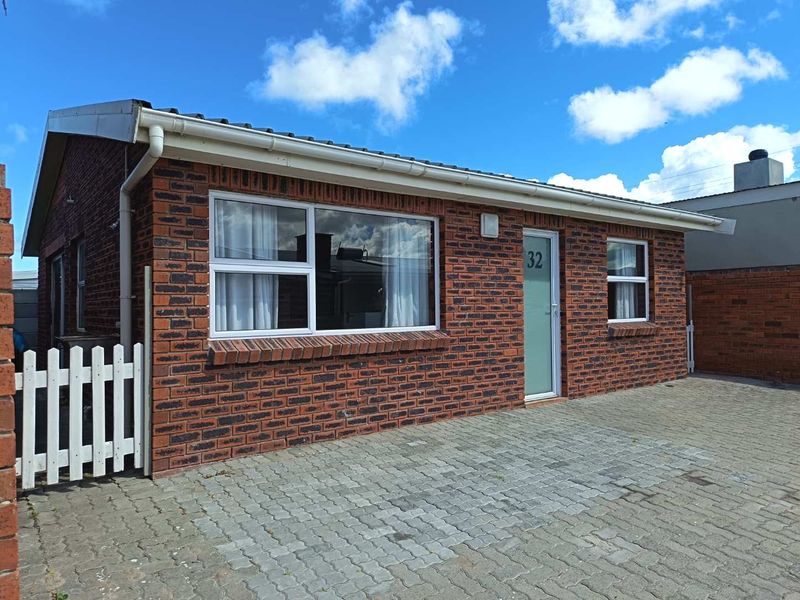 A well-maintained single-story face brick home featuring a paved driveway, white picket gate, and modern aluminium window frames.