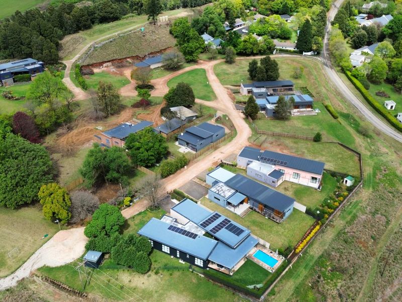 Aerial view of a residential estate featuring multiple modern dwellings, solar panel installations, a swimming pool, and expansive landscaped grounds.