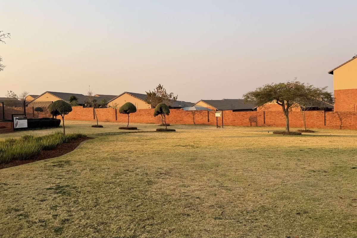 A view of a communal garden area featuring a well-maintained lawn and a brick boundary wall surrounding the residential complex.