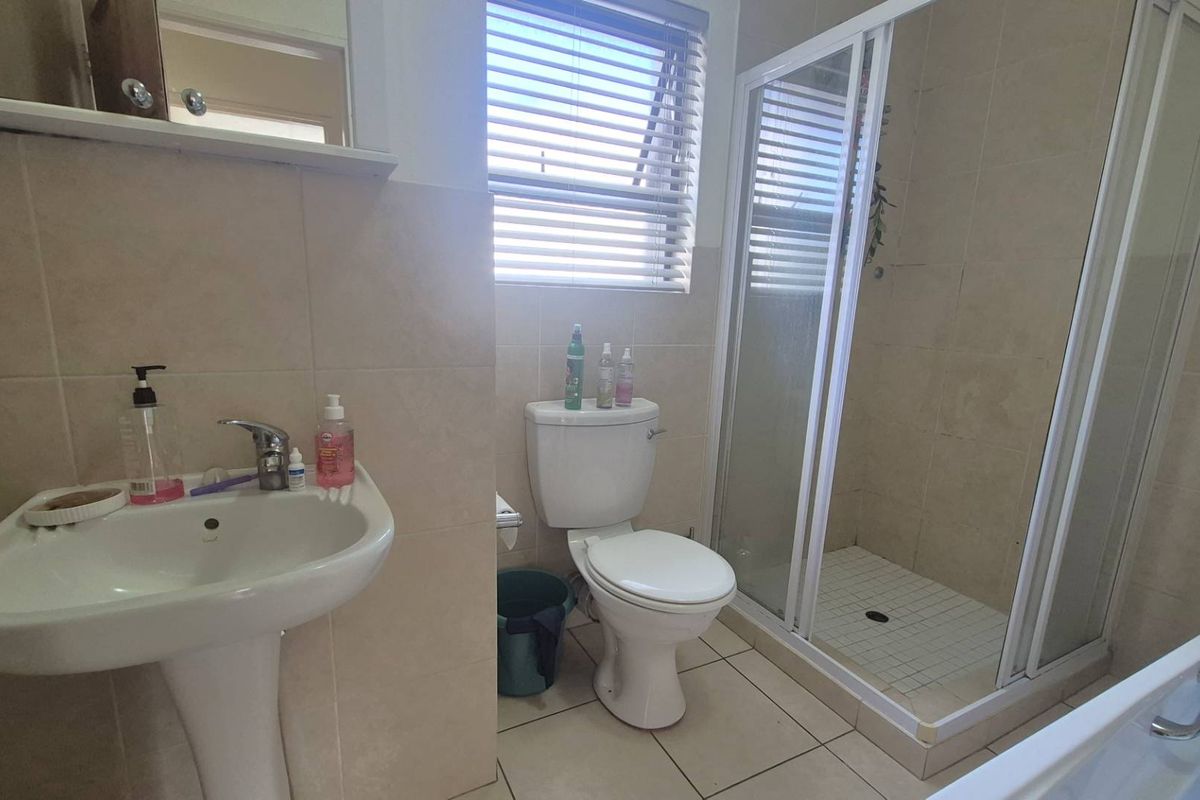 A functional bathroom featuring a pedestal basin, a white toilet, a glass-enclosed shower, and neutral wall and floor tiling.