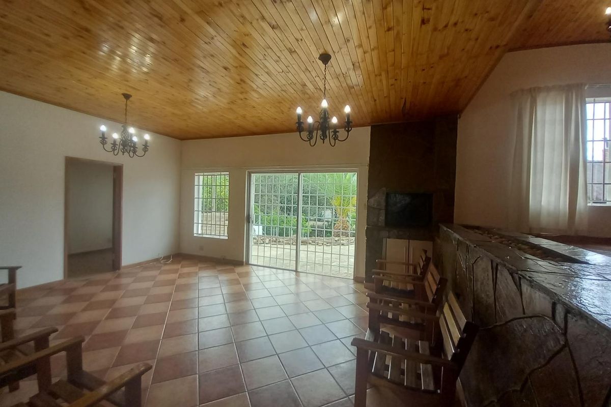 Spacious living area featuring a stone-clad fireplace, tiled flooring, and a timber-paneled ceiling with sliding glass doors leading to the outdoor patio.