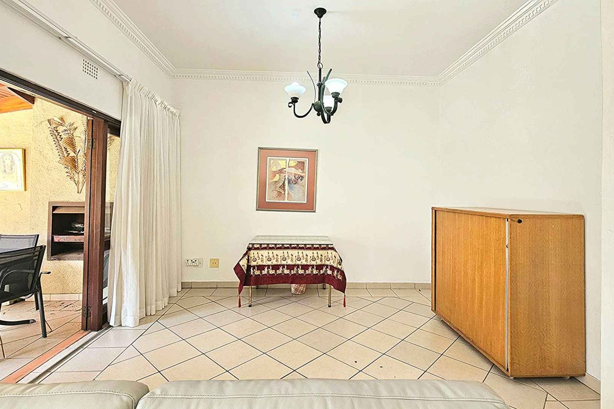 A bright living area featuring tiled flooring, decorative ceiling cornices, and large sliding doors providing seamless access to an outdoor patio space.