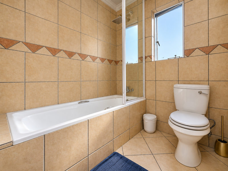 A functional bathroom featuring a built-in bathtub with a glass shower screen, tiled finishes, and a standard toilet.
