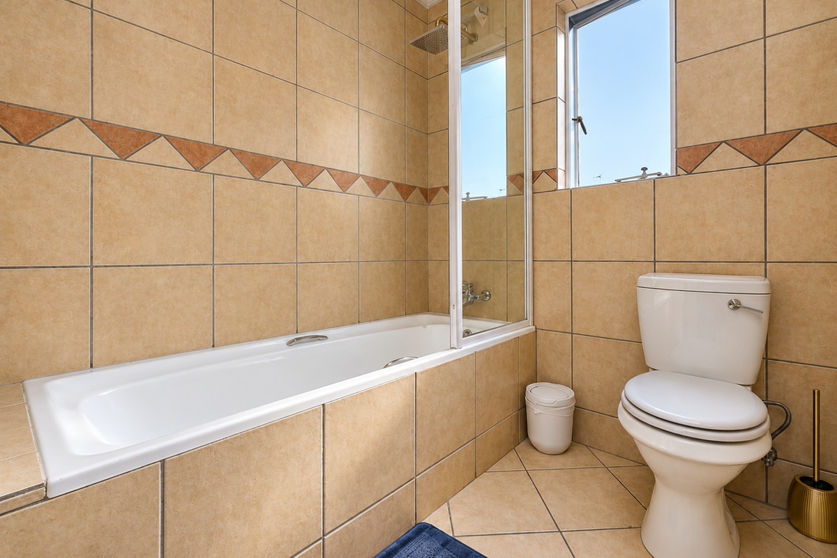 A functional bathroom featuring a built-in bathtub with a glass shower screen, tiled finishes, and a standard toilet.