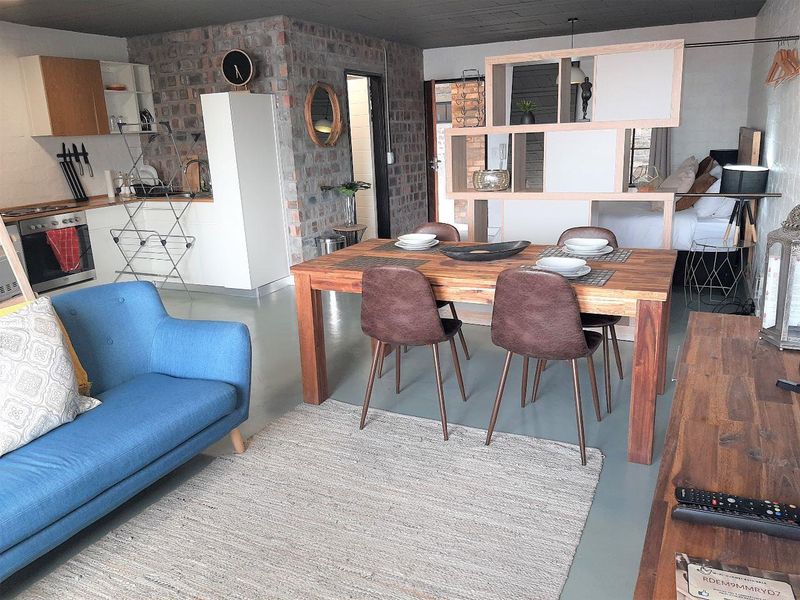 An open-plan apartment living space featuring an exposed brick wall, integrated kitchen cabinetry, and a functional room divider separating the sleeping area.