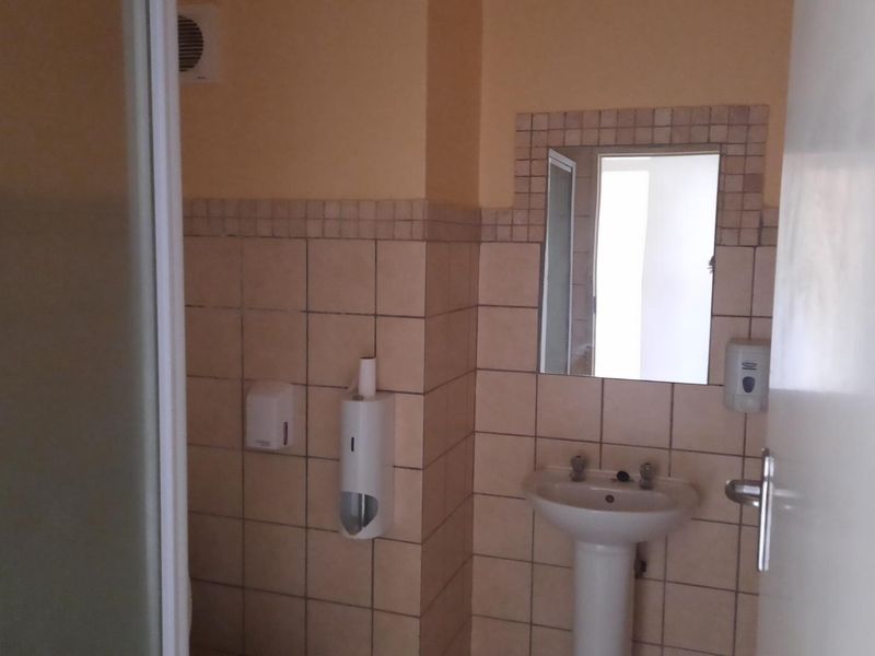 A functional bathroom featuring a pedestal basin, tiled splashback, wall-mounted mirror, and a shower enclosure.