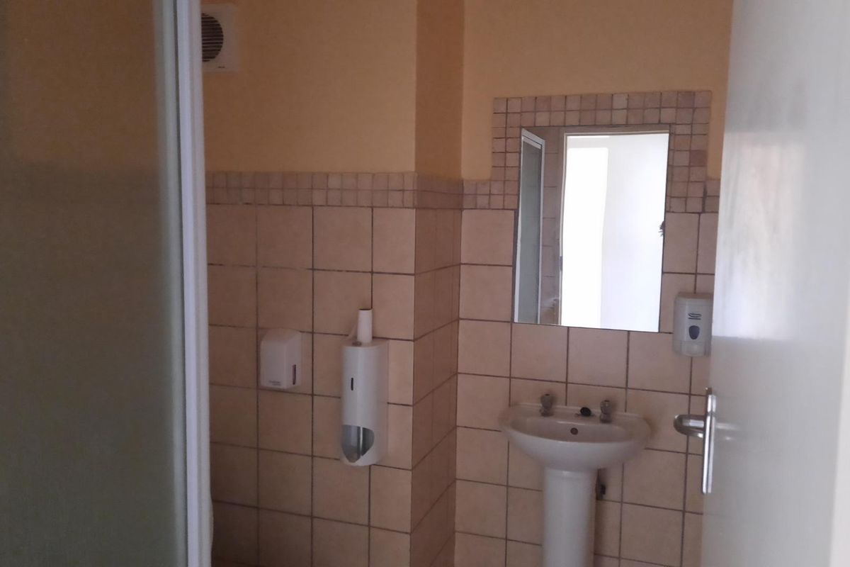 A functional bathroom featuring a pedestal basin, tiled splashback, wall-mounted mirror, and a shower enclosure.