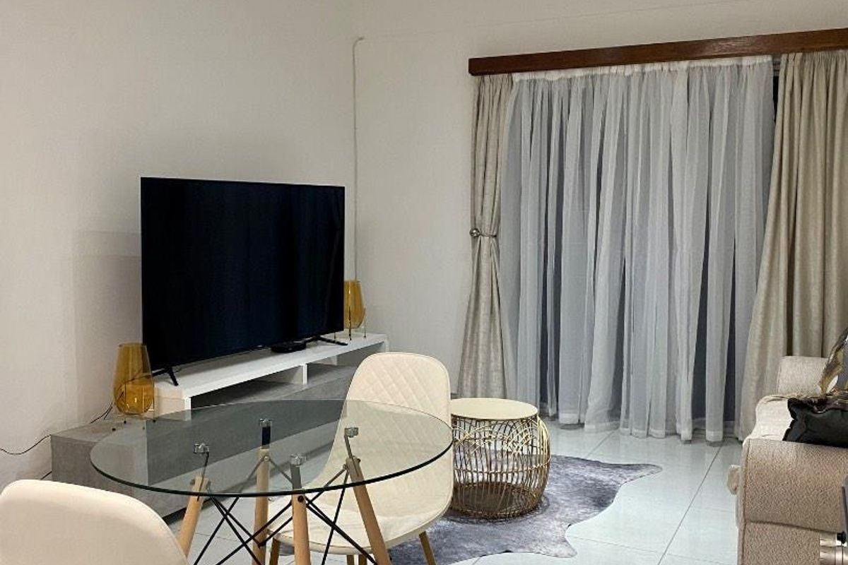A bright living room featuring large format floor tiles, recessed ceiling downlights, and a sliding door with curtain tracks leading to an outdoor area.