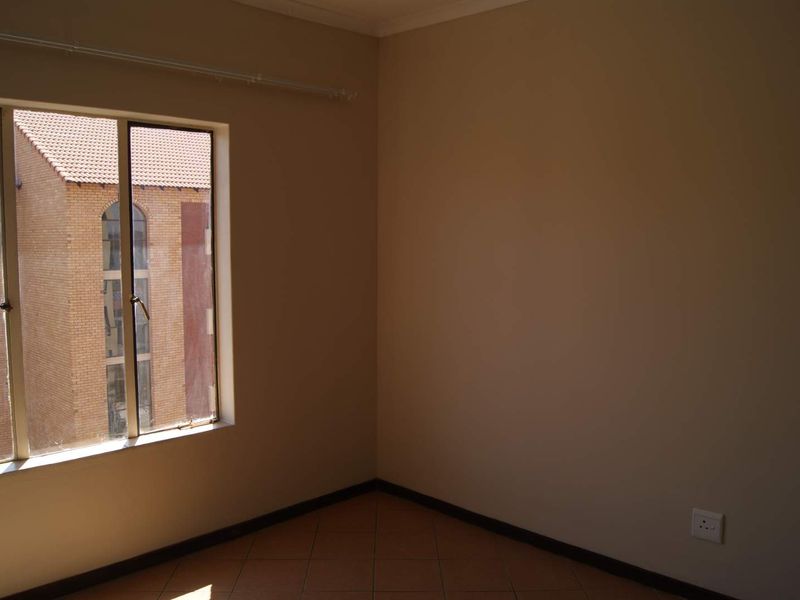 An empty bedroom featuring tiled flooring, neutral walls, and a window with a view of the neighboring building.