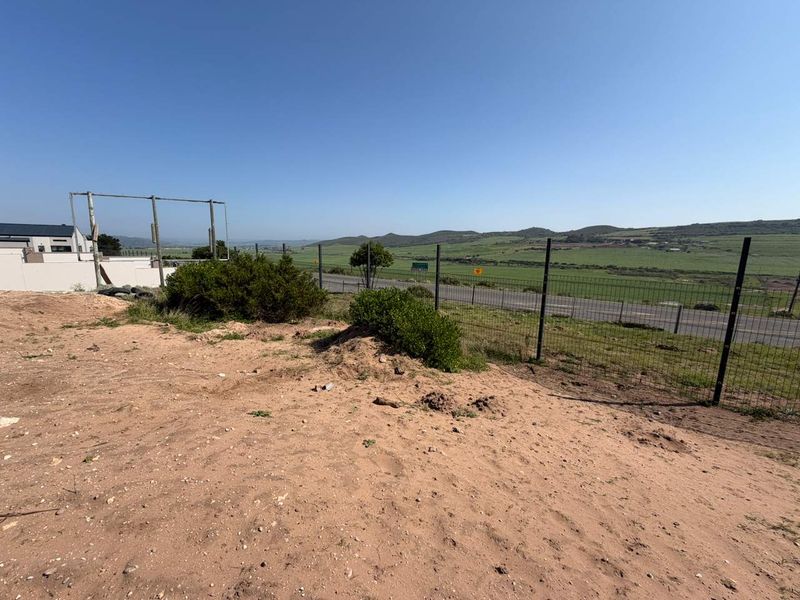 A view of a vacant residential plot featuring wire mesh perimeter fencing and an open, undeveloped landscape with distant rural views.