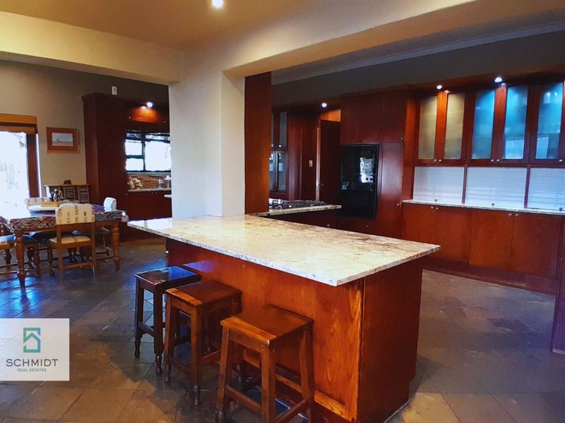 Spacious open-plan kitchen and dining area featuring warm wooden cabinetry, granite countertops, a central island, and durable stone flooring.