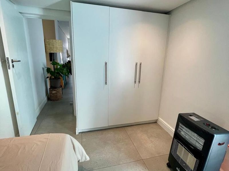 A bedroom featuring modern tiled flooring, recessed downlighting, and a clean, white built-in wardrobe providing ample storage space.