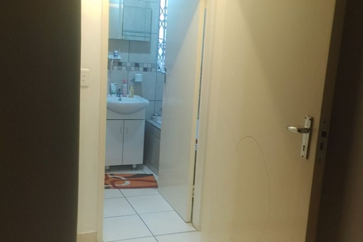 A view through a doorway into a functional bathroom featuring a vanity cabinet, basin, and tiled finishes.