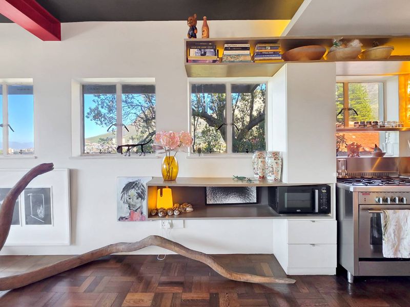 Modern kitchen area featuring built-in cabinetry, stainless steel oven, gas hob, and warm integrated shelving, set against rich parquet flooring with scenic window views.