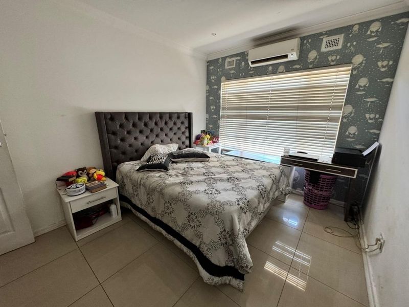 A bedroom featuring tiled flooring, a split-system air conditioner, and a decorative wallpaper feature wall with venetian blinds.