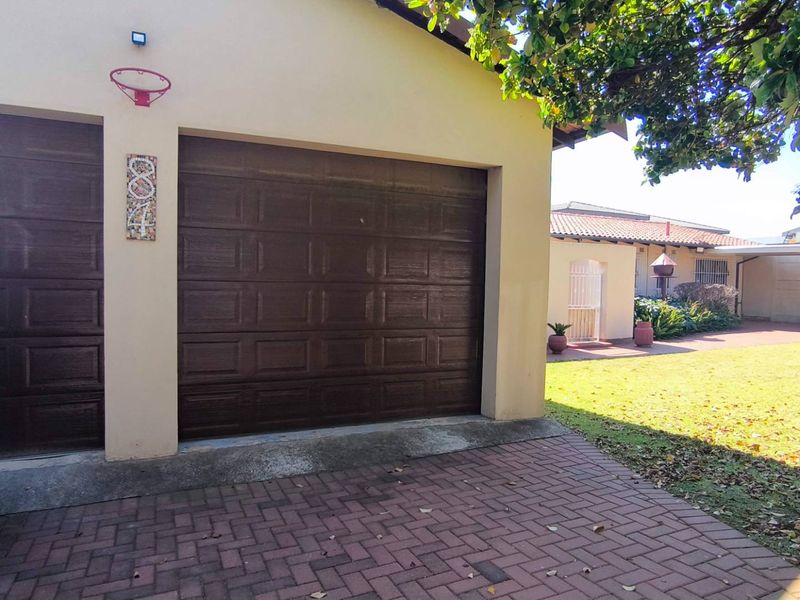 Front view of the property featuring a double garage with brown sectional doors, a paved driveway, and a well-maintained lawn area.