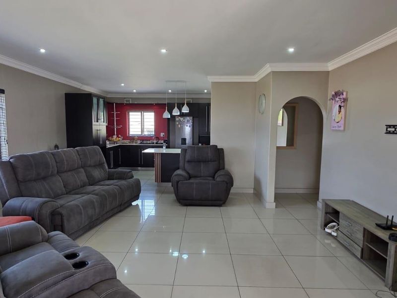 Spacious open-plan living area featuring large porcelain floor tiles, recessed lighting, and a modern kitchen with a central island and dark cabinetry.