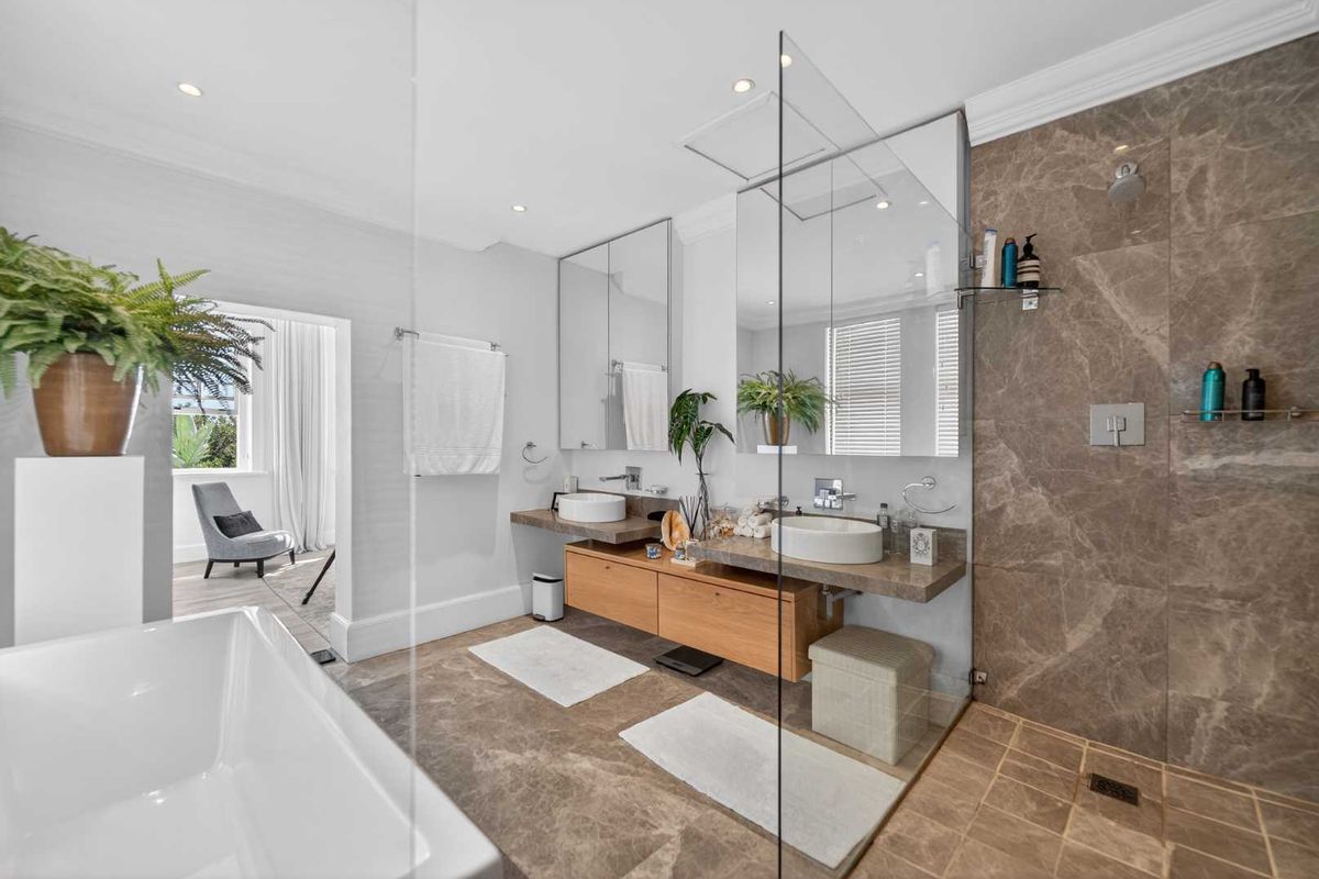 Modern luxury bathroom featuring a freestanding bathtub, walk-in shower with stone tiling, and a double vanity with vessel sinks and wall-mounted cabinetry.