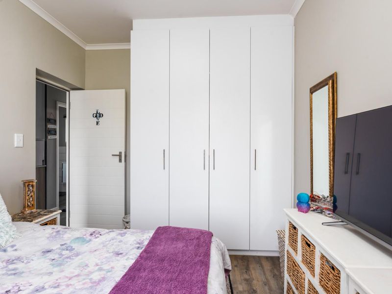 A well-maintained bedroom featuring modern white built-in wardrobes, laminate flooring, and neutral wall tones.