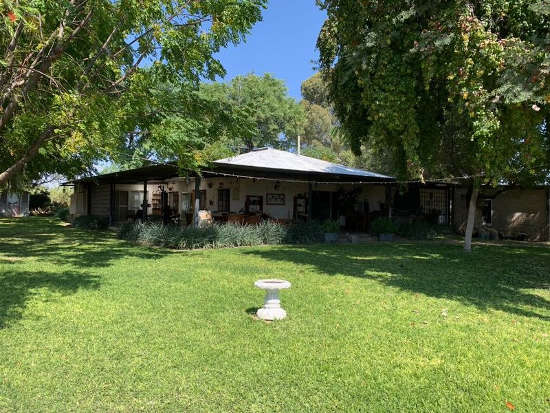 A view of the rear elevation of the farmhouse, featuring a wide covered patio area overlooking a spacious, well-maintained garden with mature trees.