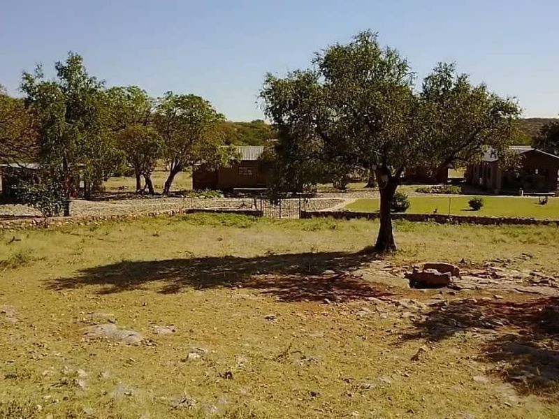 A wide view of the farm property grounds featuring mature trees, a stone boundary wall, and a metal gate leading to the main buildings.
