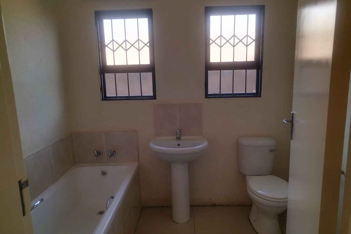 A functional bathroom featuring a pedestal basin, bathtub, and toilet, with tiled finishes and security bars on the windows.