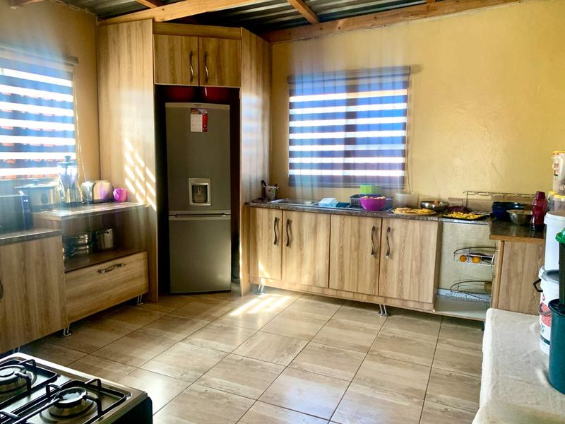A functional kitchen featuring wood-look laminate cabinetry, tiled flooring, and exposed timber ceiling beams, providing a practical workspace with ample storage.