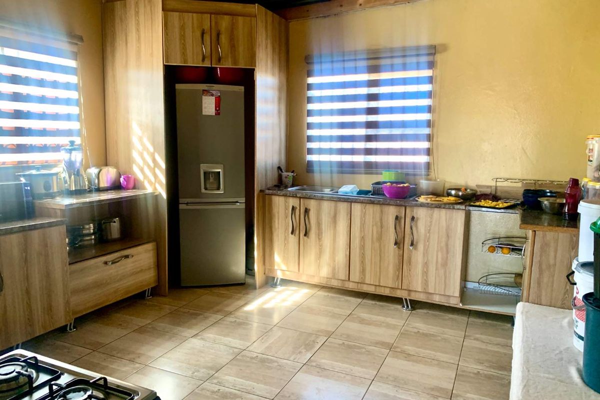 A functional kitchen featuring wood-look laminate cabinetry, tiled flooring, and exposed timber ceiling beams, providing a practical workspace with ample storage.