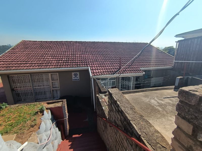 Rear exterior view of the property featuring a tiled roof, concrete stairs with a handrail, and a retaining wall structure.