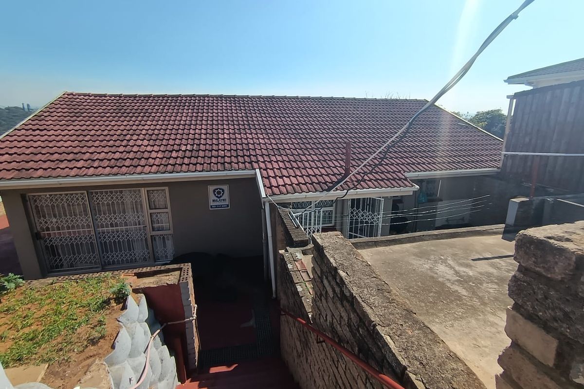 Rear exterior view of the property featuring a tiled roof, concrete stairs with a handrail, and a retaining wall structure.