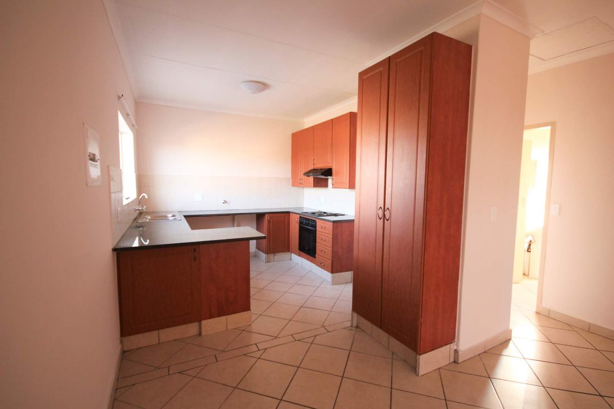 A functional kitchen featuring wooden cabinetry, granite countertops, a built-in oven, hob, extractor fan, and tiled flooring in an open-plan layout.