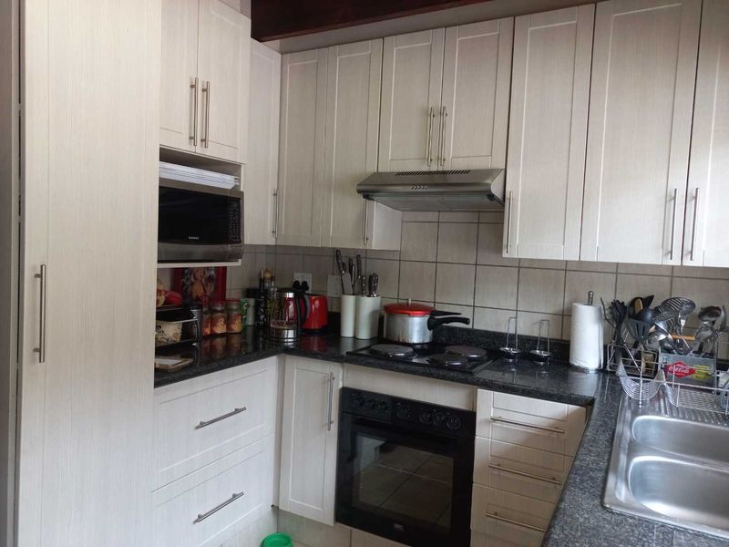 A functional kitchen featuring light-toned cabinetry, granite countertops, a built-in oven, electric hob, and a double bowl sink with tiled backsplash.