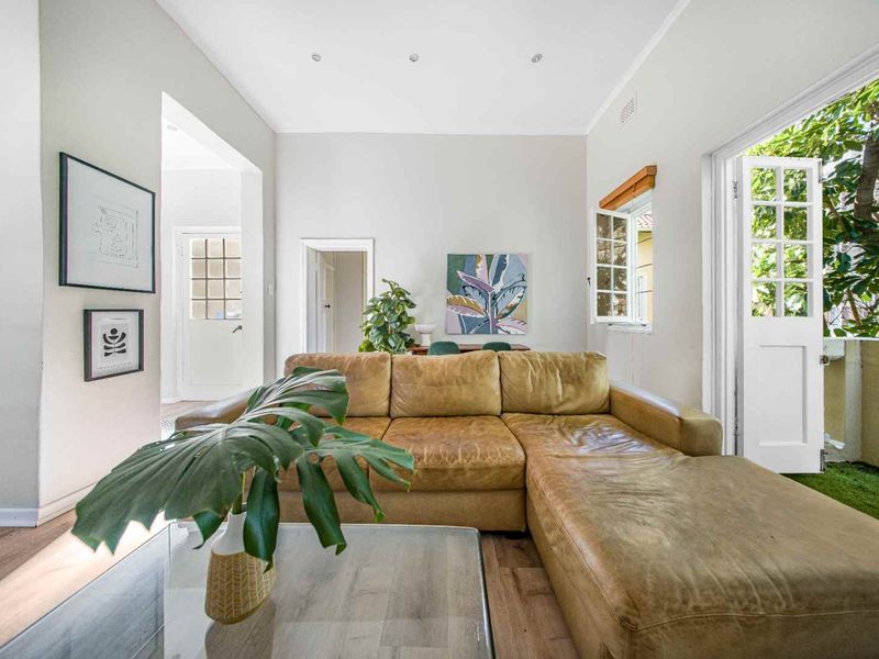 Bright living room featuring laminate flooring, recessed downlights, and direct access to an outdoor balcony through classic white french doors.