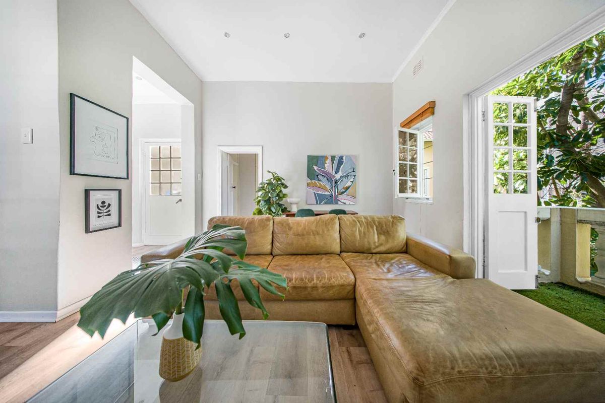 Bright living room featuring laminate flooring, recessed downlights, and direct access to an outdoor balcony through classic white french doors.