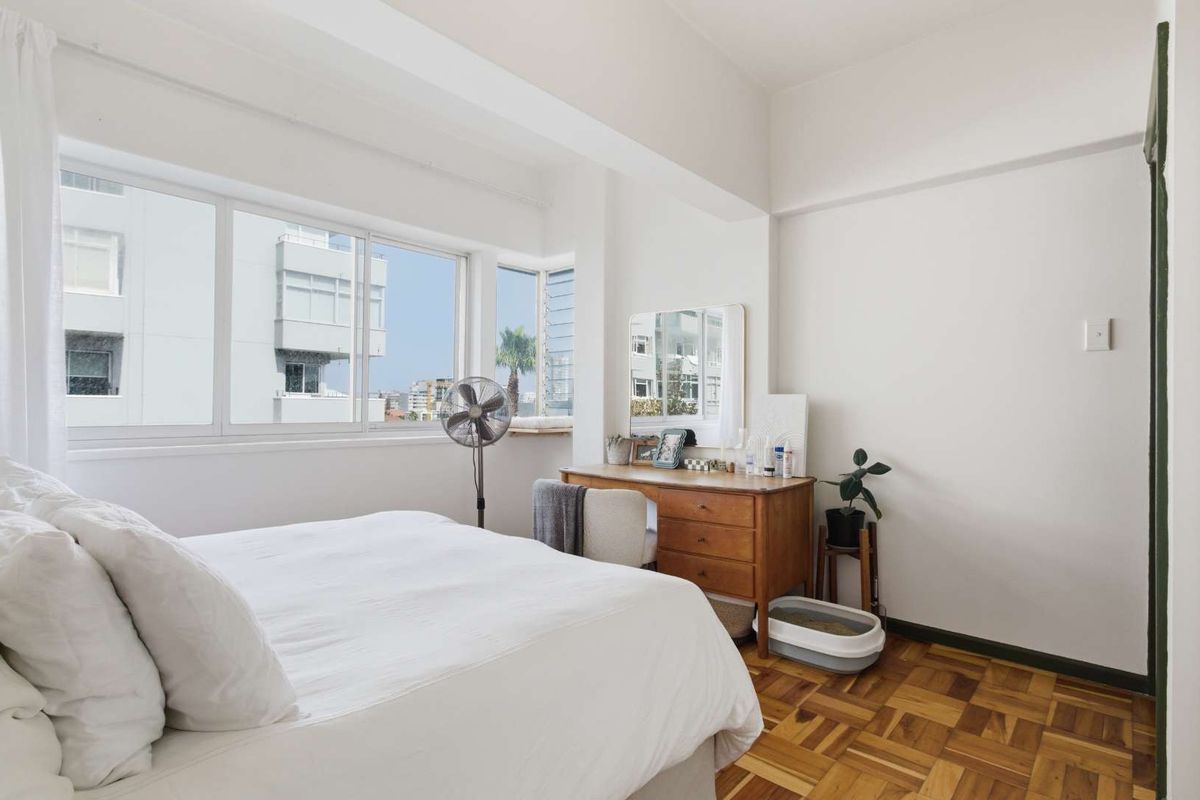 A bright bedroom featuring classic parquet flooring and large windows that provide ample natural light and urban views.