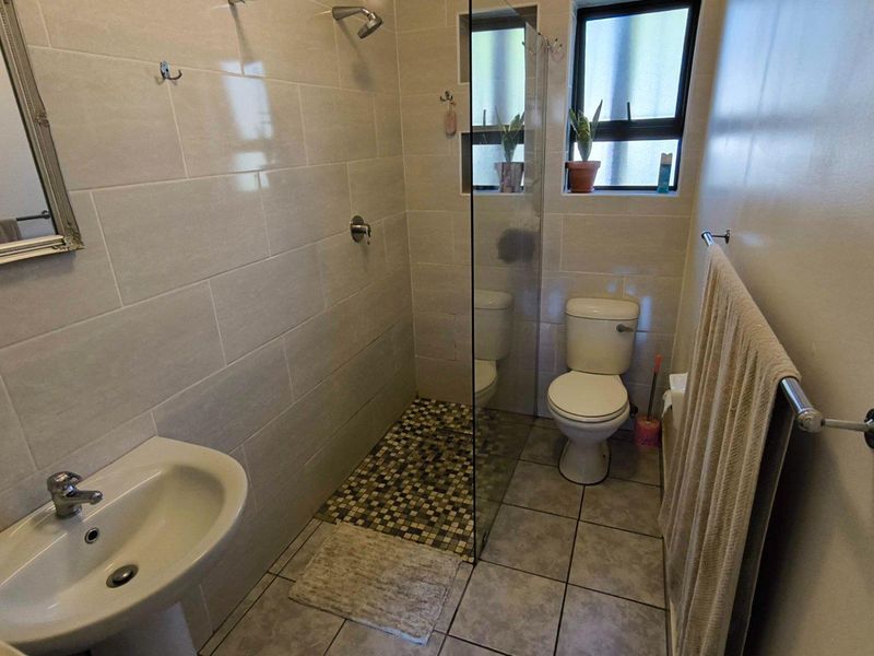 A functional bathroom featuring a pedestal basin, a walk-in shower with a glass screen and mosaic floor tiling, and a standard toilet.