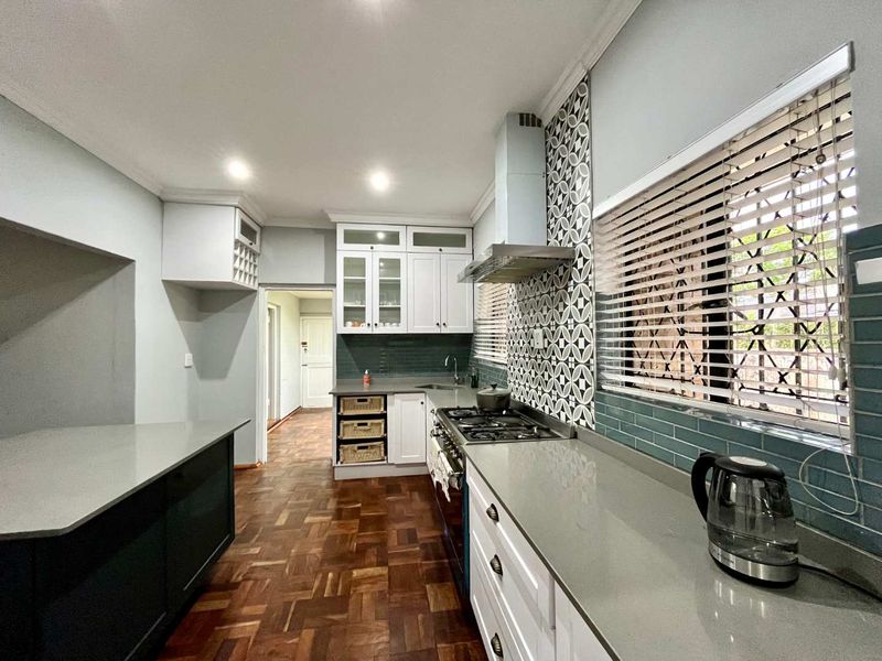 Modern kitchen featuring white cabinetry, stone countertops, gas hob with extractor, and stylish patterned tile backsplash, complemented by warm parquet flooring.