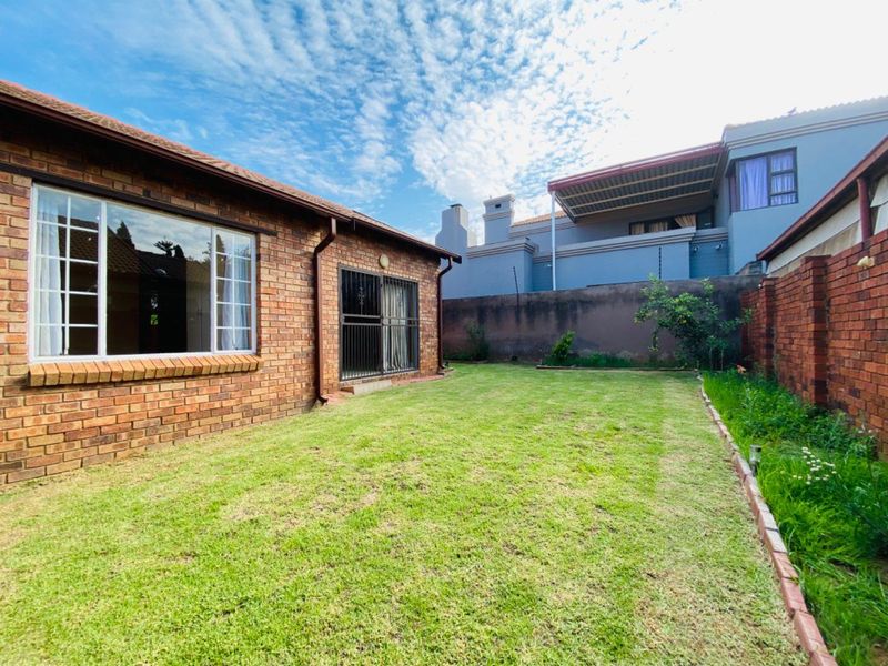 A private rear garden featuring a face brick exterior, a lawn area, and secure boundary walls with electric fencing.