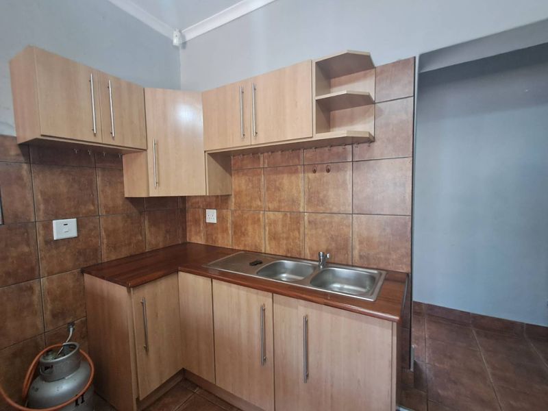 A functional kitchen featuring light wood-tone cabinetry, a double stainless steel sink, and brown tiled splashbacks, offering a practical layout for culinary tasks.