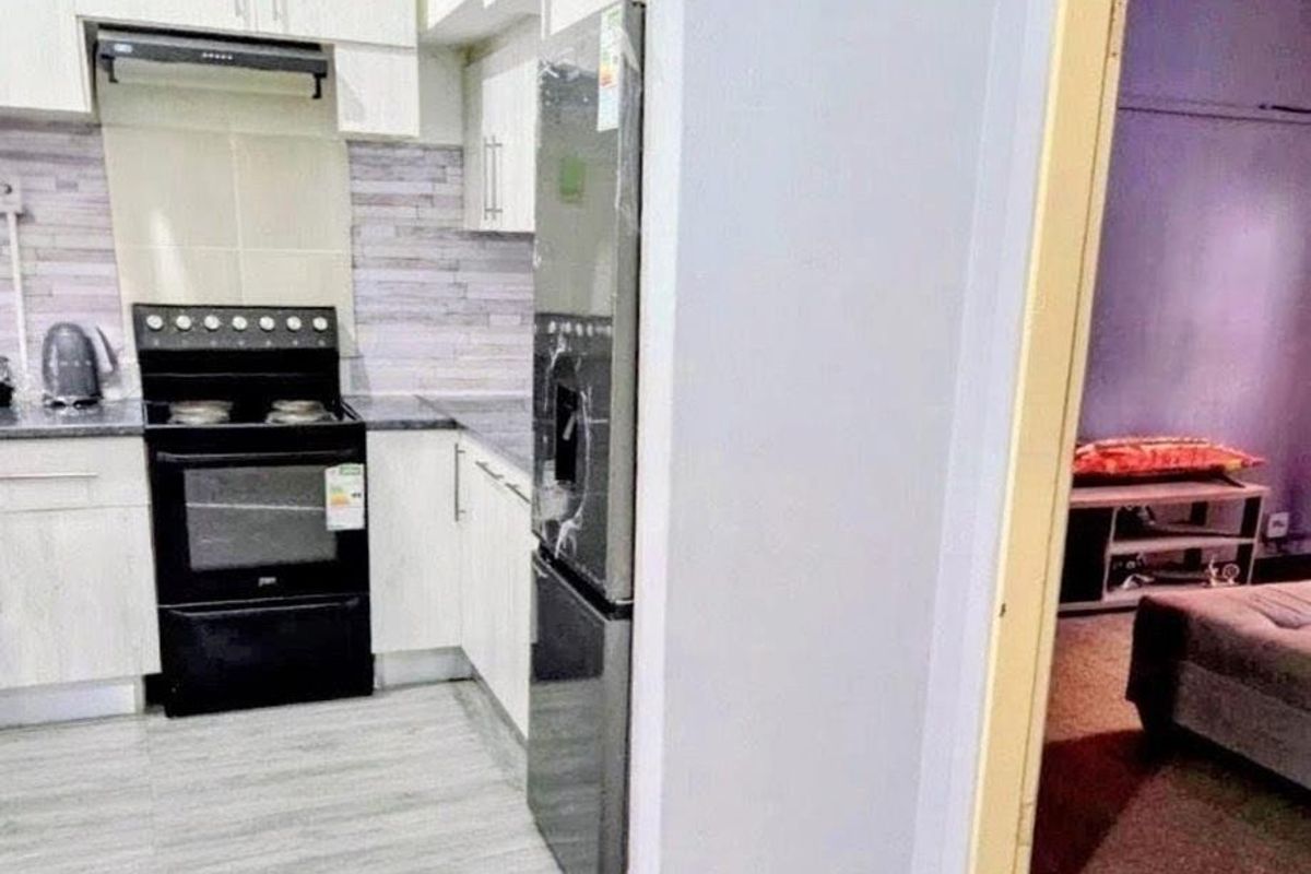 Compact kitchen featuring built-in cabinetry, a modern stove with extractor fan, and tiled backsplash, with an adjacent view into a bedroom area.