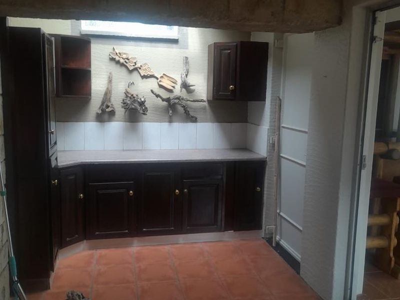 A functional scullery or utility area featuring dark wood built-in cabinetry, stone countertops, tiled backsplash, and terracotta floor tiles.