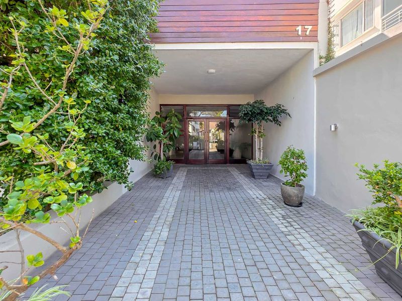 A well-maintained front entrance featuring a paved driveway, glass double doors, and timber cladding detail.